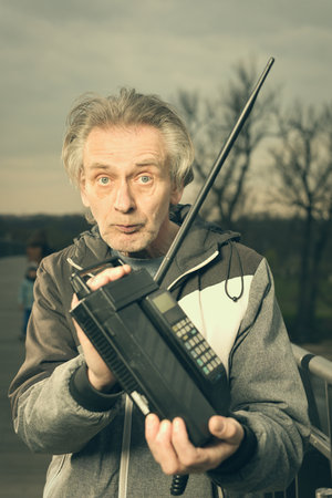 Older man outdoor on bridge using retro cellphone to callの写真素材