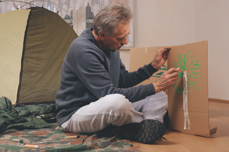 Older man in senior age relaxing in apartment room in tent instead of outdoor campingの写真素材