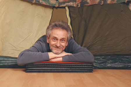 Older man in senior age relaxing in apartment room in tent instead of outdoor camping