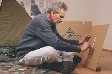 Older man in senior age relaxing in apartment room in tent instead of outdoor camping