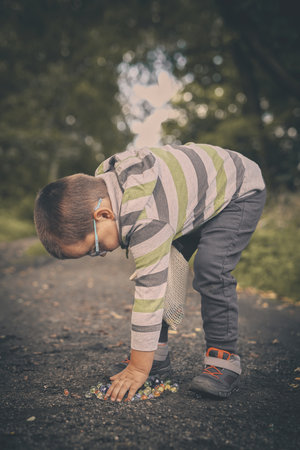 Little boy on dusty path training classic marbles outdoor on pathway in nature