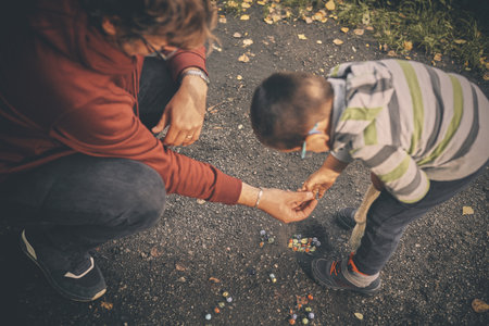 Adult man and his son training classic marbles outdoors on pathway in nature