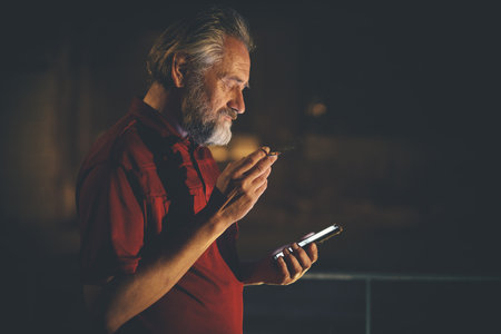 Older man in red shirt waiting for something and using mobile phone on night city location