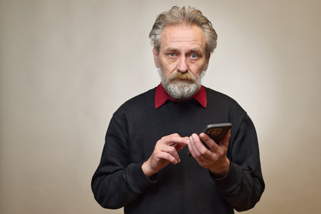 Old man over 60 portrait in studio with smartphoneの写真素材