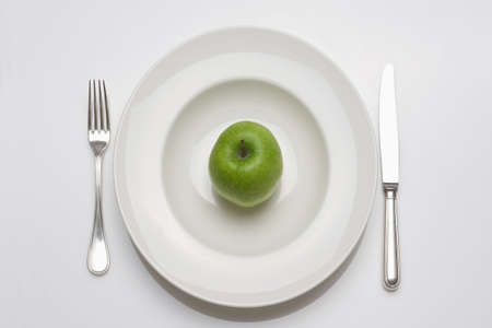 diet - green apple on a white plate with knife and forkの写真素材