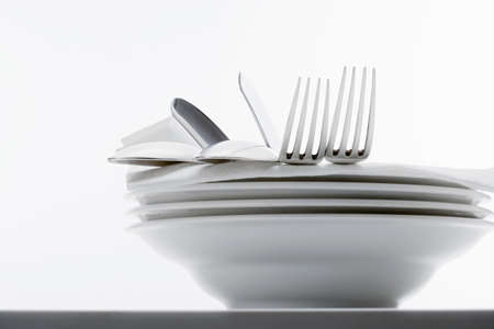 closeup of silverware on pile of plates with white clothの写真素材