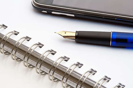extreme closeup of a fountain pen, spiral notebook and cell phoneの写真素材
