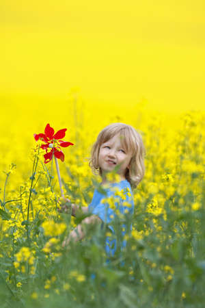 boy with long blond hair holding pinwheel in canola fieldの写真素材