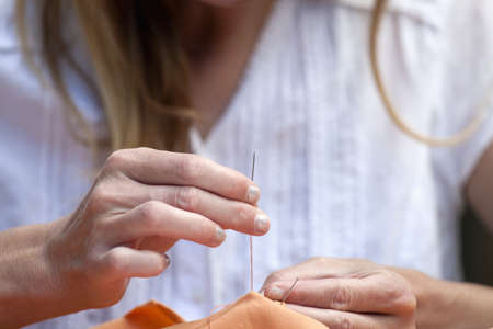 closeup of womans hands sewing orange cloth outdoorsの写真素材