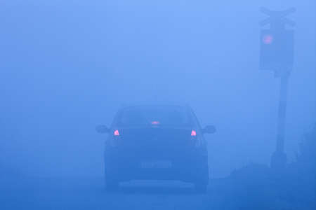 car waiting at rural railroad crossing with red lights blinking in fogの写真素材