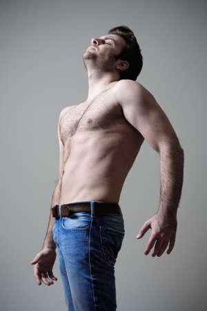 young shirtless musculous man in jeans standing - isolated on gray