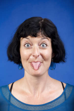 middle-aged woman sticking out her tongue - isolated on blueの写真素材