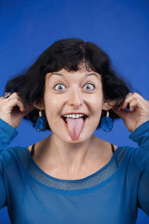 woman sticking out her tongue and pulling her ears - isolated on blue