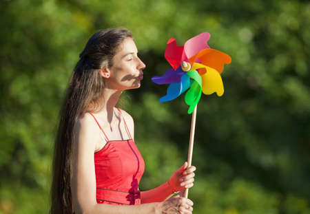 woman with long hair holding a multicolored pinwheel in a park の写真素材