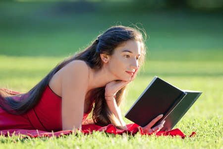 woman with long hair in red dress reading a book in a parkの写真素材