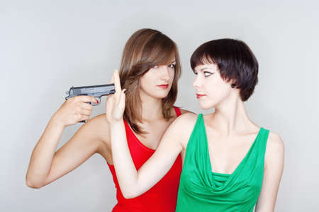 two young female friends playing with a gun - isolated on grayの写真素材
