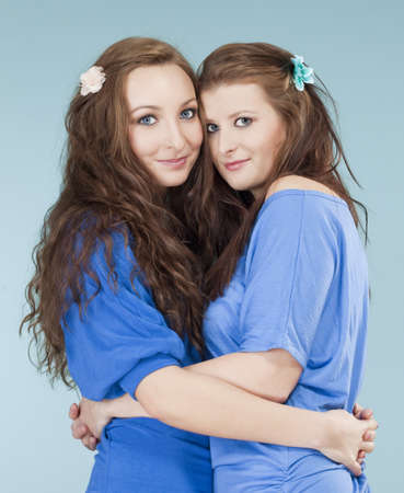 two young female friends hugging, looking - isolated on blueの写真素材