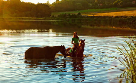 Woman with Two Horses in a Lake at Sunsetの写真素材