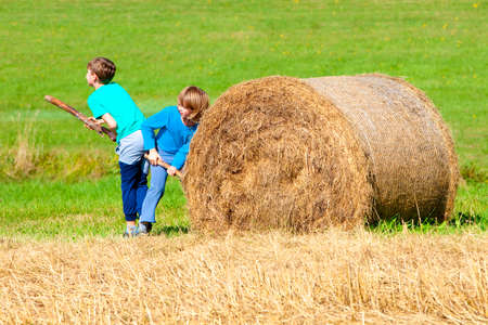 Two Boys Moving Bale of Hay with Stick as a Leverの写真素材