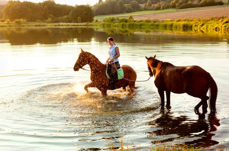 Woman with Two Horses in a Lake at Sunsetの写真素材