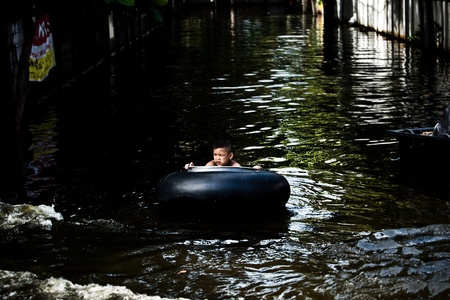 BANGKOK - NOVEMBER 13: An unidentified male child floats on a tire tube in the flooded area at Bang Khen road during the massive flood crisis on November 13, 2011 in Bangkok. のeditorial素材