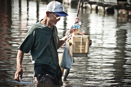 BANGKOK - NOVEMBER 13: An unidentified man carries a meal box and walk across a road in the flooded area at Kaset - Navamin road during the massive flood crisis on November 13, 2011 in Bangkok. のeditorial素材