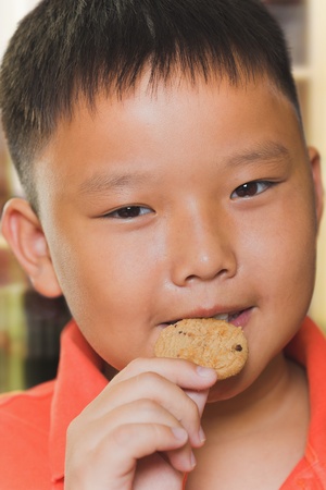 Young asian boy eats a piece of biscuitの写真素材