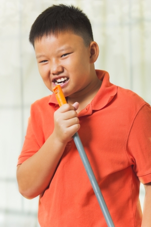 Young asian boy holds a broomstick as a microphone for singingの写真素材