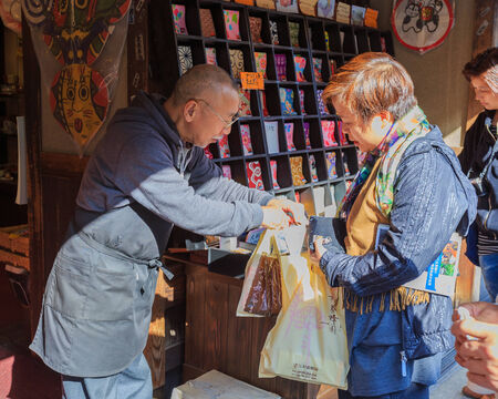 FUKUOKA, JAPAN - NOVEMBER 13: Souvenir business in Fukuoka, Japan on November 13, 2013. Unidentified Japanese souvenir shop keeper in front of Dazaifu Tenmangu hands souvenir bags to his customerのeditorial素材