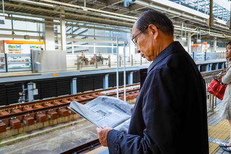 NAGOYA, JAPAN - NOVEMBER 22 2015: Unidentified Japanese train commuter reads a newspaper while waits for a Shinkansen train on a platform at Nagoya stationのeditorial素材