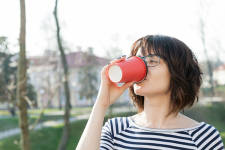 A girl in a striped T-shirt is drinking coffee with a blurred backgroundの写真素材