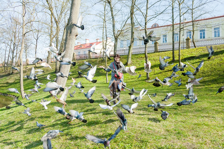 A girl in a gray coat, runs through a flock of pigeons on the lawn on a sunny dayの写真素材