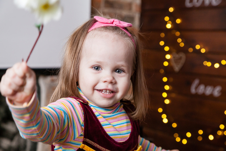 little cheerful girl with flower on blurred background with lightsの写真素材
