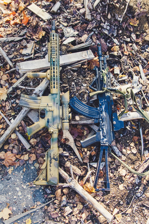 Assault rifles lie on wooden chips and fallen leavesの写真素材