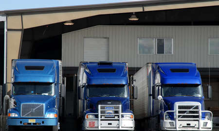 three blue semi truck tractors at loading dock