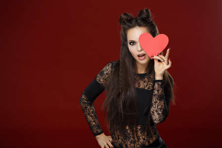 Beautiful long-haired brunette holding a red heart. Studio, dark backgroundの写真素材