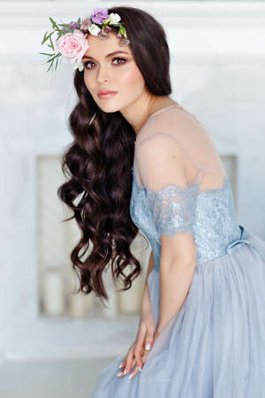 Portrait of a beautiful sexy brunette girl with brown eyes in a delicate dress and a wreath of flowers on her headの写真素材