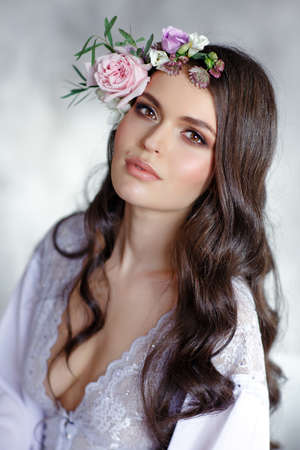 Portrait of a beautiful sexy brunette girl with brown eyes in a delicate dress and a wreath of flowers on her headの写真素材