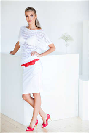 Beautiful and sensual blonde girl in a white dress standing at the white cube in the Studioの写真素材