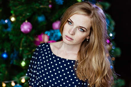 Portrait of a beautiful girl with freckles and blue eyes on the background of the Christmas treeの写真素材