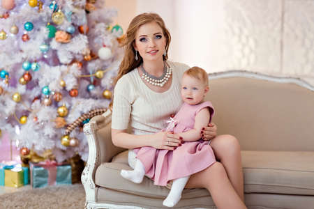 Mother and daughter in bright clothing against a white Christmas tree sitting on the couchの写真素材