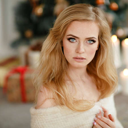 Portrait of blond, sensual , blue-eyed girl with freckles in a white fur Cape on the Christmas tree, close-upの写真素材