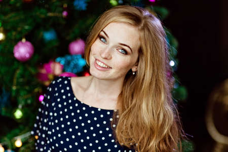 Portrait of red-haired beautiful girl with freckles in a blue dress with polka dots on a background of colored lightsの写真素材