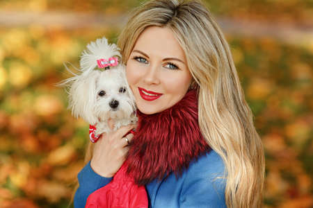Luxury blonde girl with beautiful hair in autumn coat holding a small dog in her arms, close-up