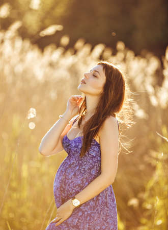 Beautiful tender pregnant woman smiles and enjoys a sunny summerの写真素材