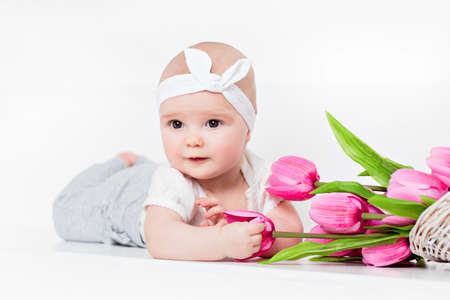 Small very cute wide-eyed smiling baby girl lying on her tummy on a white background in the Studio and keeps handles tulipsの写真素材