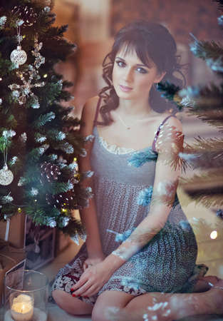 Beautiful sexy brunette girl in a grey dress sitting near the Christmas treeの写真素材