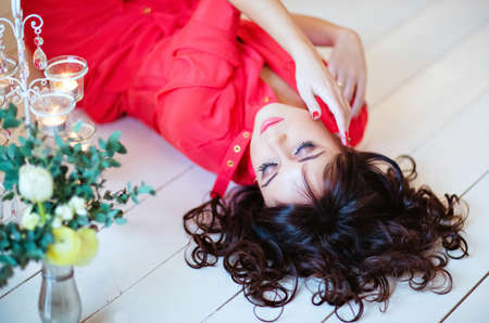Beautiful girl with closed eyes in a red dress lying on the floorの写真素材