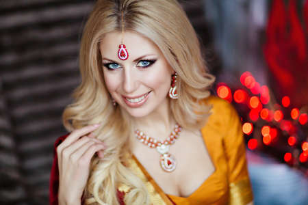 Beautiful and sensual blonde girl in Indian red saree on the background of red lights, close upの写真素材