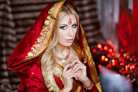 Beautiful and sensual blonde girl in Indian red saree and the hood sits on a background of red lightsの写真素材